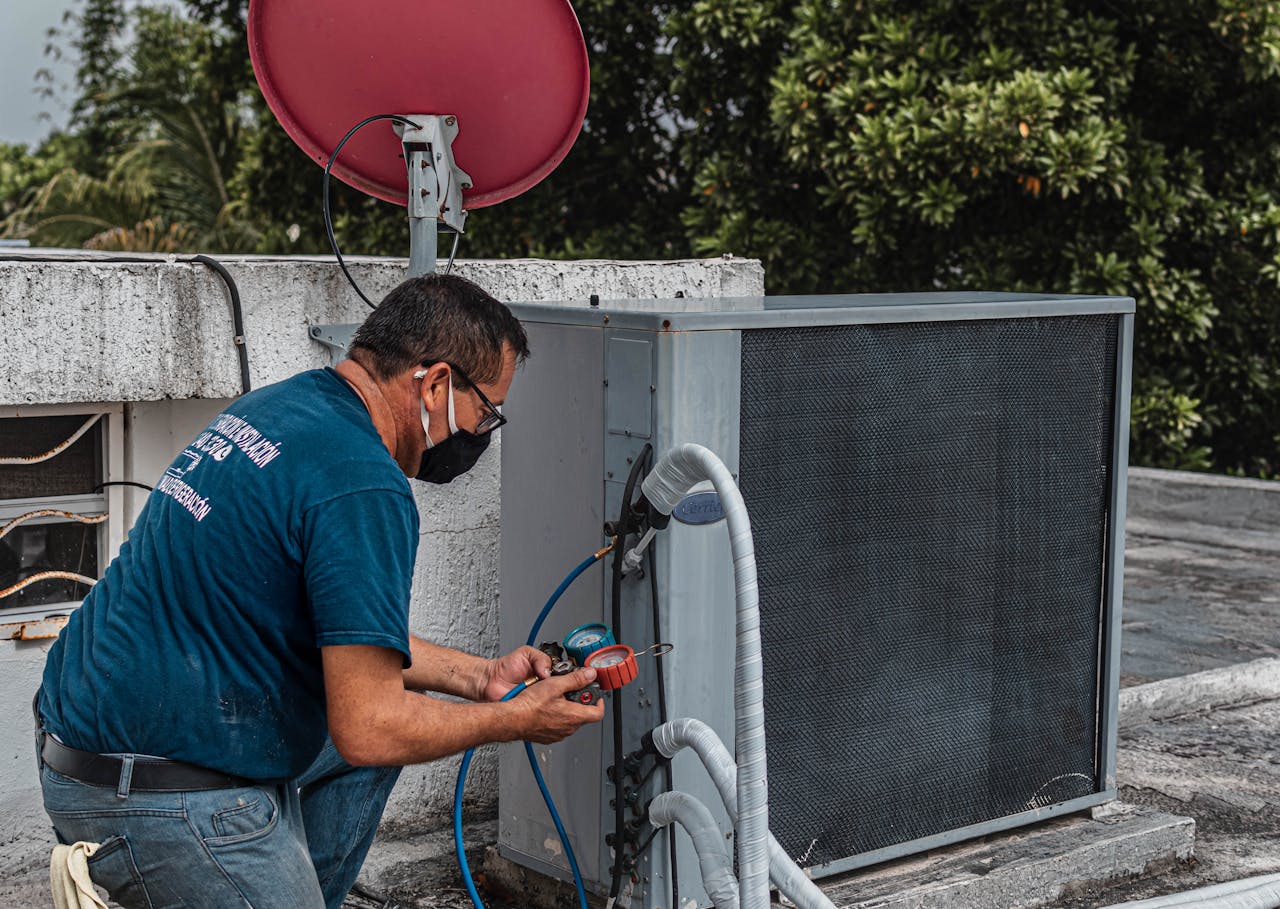 portfolio-01 Technician repairing an air conditioner unit outdoors, wearing a facemask and using a manifold gauge.
